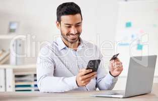 Young mixed race happy businessman using a credit card and phone to shop online at work. One hispanic man paying for a purchase using his cellphone. Man buying products using his phone and bank card