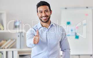 Young happy handsome mixed race businessman showing a thumbs up standing in an office alone at work. One pleased hispanic male boss smiling expressing support and agreement with a thumb up