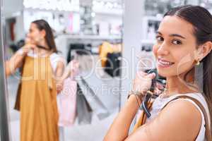 Portrait of a trendy young woman holding a dress against her deciding whether to buy it. Smiling female fitting on clothes in a store. Mixed race shopper happy about finding a sale and discount