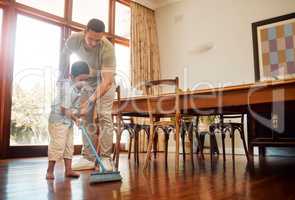 Mixed race father helping little boy sweep dust and dirt on wooden floor with broom for household chores at home. Cute boy helping dad with daily spring cleaning tasks. Kid learning to be responsible