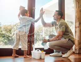 Young happy mixed race father and son giving each other a high five while cleaning at home. Little hispanic boy helping his dad wash windows. Parent and child joining hands to celebrate achievement