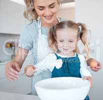 Mother and daughter baking at home. Happy mother and child bonding and cooking. Woman helping her daughter make batter. Young mother holding an egg, baking with her little girl.