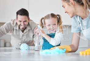 Happy family cleaning the kitchen together. Little girl spraying disinfectant from a bottle. Caucasian family cleaning the kitchen counter together. Mother and father bonding with their daughter