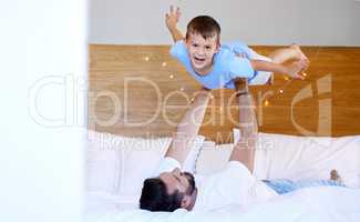 Caucasian father lifting his cute little son in the air to pretend to fly like a plane or superhero with arms out on a bed at home. Loving dad playing and bonding with cheerful kid in the morning