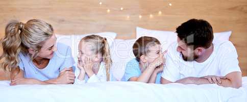 Happy carefree caucasian family lying cosy on bed while bonding together at home. Loving parents spending quality time with little son and daughter. Cute kids enjoying lazy morning with mom and dad