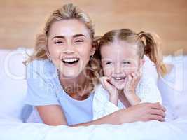 Happy caucasian mother and daughter lying on a bed at home. Cheerful woman with cute little girl enjoying a cosy and lazy relaxing day together. Loving parent bonding and sharing quality time with kid