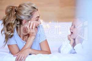 Happy caucasian mother and daughter lying on a bed at home. Cheerful woman with cute little girl enjoying a cosy and lazy relaxing day together. Loving parent bonding and sharing quality time with kid