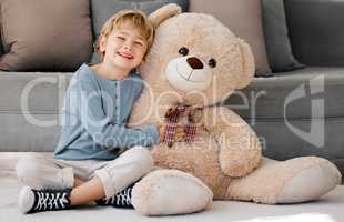 Portrait of one happy little caucasian boy smiling while hugging a big and cosy fluffy teddy bear on the floor in the lounge at home. Adorable kid relaxing and playing with soft stuffed toy alone