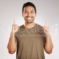 Handsome young mixed race man pointing towards copyspace while standing in studio isolated against a grey background. Happy hispanic male advertising or endorsing your product, company or idea