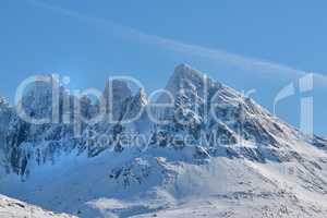 A cold mountain peak covered in snow during winter with a blue sky background. Beautiful landscape of a snowy summit with freezing weather conditions in the morning outdoors in nature