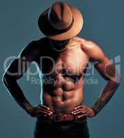 Fashionable african American model posing shirtless against blue studio background with copyspace. Sexy, unknown black man with attitude showing bare six pack while wearing hat. Masculine and muscle