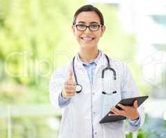 Young female Hispanic doctor wearing a labcoat and smiling while using a digital tablet and showing thumbs up in her office. Physical health is important to your wellbeing. Mixed race doctor using wireless device at her job in the hospital