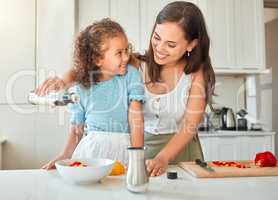 Happy mother and little daughter cooking together in the kitchen. Woman adding salad dressing while preparing a vegetarian meal with her child