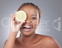 No shine on this face. Studio shot of an attractive young woman holding a sliced lemon against a grey background.