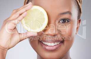 Perfectly matte skin, from her garden. Studio shot of an attractive young woman holding a sliced lemon against a grey background.