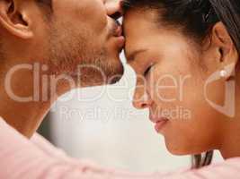 Closeup of mixed race man kissing his girlfriends forehead. Headshot of hispanic couple bonding and sharing an intimate moment at home. Beautiful woman with freckles feeling in love with boyfriend