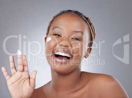 Long gone are harsh scrubs. Studio shot of an attractive young woman applying moisturiser to her face against a grey background.