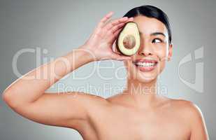 A happy mixed race woman holding an avocado. Hispanic model smiling and promoting the skin benefits of a healthy diet against a grey copyspace background