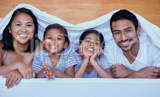 Happy family in bed. Portrait of hispanic family in bed. Young family under a bed sheet. Two parents bonding with their daughters.Sisters relaxing with their parents. Family lying in bed