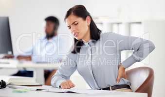 One young stressed caucasian businesswoman suffering with lower back pain in an office. Female employee feeling tense strain, discomfort and hurt to spine with poor sitting posture and long working hours at desk