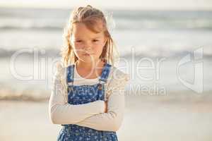 Blonde caucasian little girl with folded arms looking angry, annoyed and stubborn while spending a summer day at the beach. Cute kid expressing frustration and throwing a tantrum. Naughty bored child