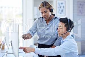 Young african american call centre telemarketing agent training new asian assistant on a computer in an office. Team leader troubleshooting solution with intern for customer service and sales support. Serious colleagues operating helpdesk together