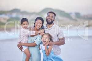 Portrait of a cheerful mixed race family laughing while standing together on the beach. Loving parents spending time with their two children during family vacation by the beach
