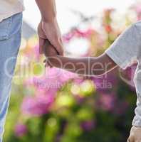 Closeup of little boy holding dads hand with nature background. African american family holding hands showing love, support and affection. A parent gives a child guidance and keep him safe