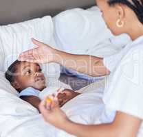 Sick little girl in bed while her mother uses a thermometer to check her temperature. Black single parent feeling daughters forehead. African American child feeling ill while her mother checks fever