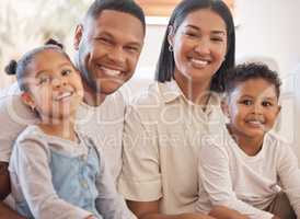 Portrait of a smiling couple with little kids at home. Mixed race mother and father bonding with their son and daughter on a weekend inside. Hispanic boy and girl enjoying free time with their parent