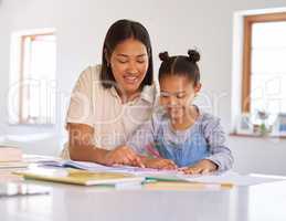 Mixed race girl learning and studying in homeschool with mom. Woman helping daughter with homework and assignments at home. Loving parent teaching happy child to colour and write at home in lockdown