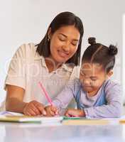 Mixed race girl learning and studying in homeschool with mom. Woman helping her daughter with homework and assignments at home. Happy parent teaching child to colour and write at home during lockdown
