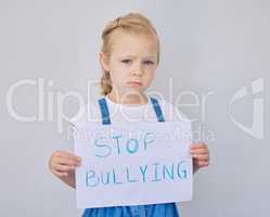 Portrait of sad little girl holding up stop bullying sign. Adorable little elementary aged girl looking sad while protesting against bullying