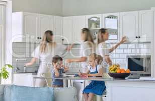 Busy mom feeding kids and cleaning the house. Little girl and boy sitting and doing homework while mother does chores. Young single parent having a nervous breakdown and looking overwhelmed