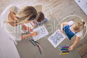 Above shot of little girl and boy sitting at table with colourful pencils and pictures while colouring with mom helping. Caucasian mother with two kids enjoying educational pastime and being creative