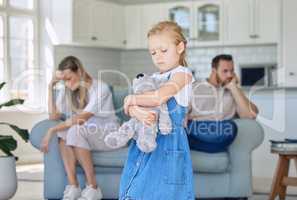 An upset little girl squeezing her teddy bear while looking sad and depressed while her parents argue in the background. Thinking about her parents breaking up or getting divorced is causing stress