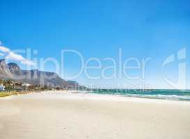 Copy space at sea with a clear blue sky and mountain in the background. Calm ocean waters washing onto an empty beach shore. Peaceful scenic coastal landscape for a relaxing and zen summer getaway