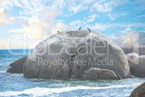 Scenic view of a beach with rocks or boulders and sea water. The landscape of a rocky coastline in spring. A big rock in the middle of the ocean with birds on it and blue sky background in summer.