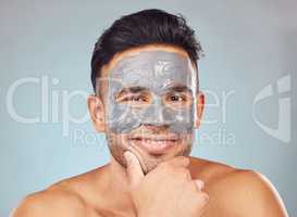 Portrait of one handsome young indian man applying an anti aging facial mask against a blue studio background. Mixed race guy wearing a moisturising clay or charcoal cream product on his face to get rid of blackheads for healthy, smooth and soft skin