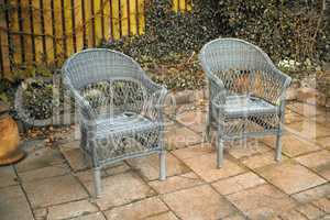 Two rattan chairs in a garden patio or terrace on a sunny day in autumn. Rustic outdoor furniture in a calm and peaceful environment surrounded by nature. Cosy spot to enjoy a break with fresh air