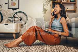 Beautiful mixed race woman using blogging laptop and cellphone to talk to clients in home living room. Hispanic entrepreneur sitting cross legged alone on lounge floor and networking on technology