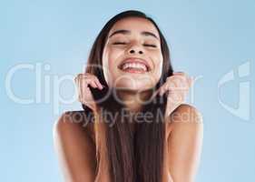 One beautiful young hispanic woman touching her sleek, silky and healthy long hair while smiling against a blue studio background. Confident and happy mixed race model with flawless complexion and natural beauty