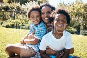 Adorable african american boys sitting on their mothers lap outside. Carefree african american family spending time outdoors at the park or their backyard. Mom embracing two sons