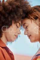 two young mixed race female friends embrace and smiling outside on a sunny day. A Beautiful gay hispanic woman with a cool afro hair style being affectionate with her asian partner