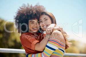 Portrait of two young mixed race female friends embracing each other and smiling outside on a sunny day. A Beautiful gay hispanic woman with a cool afro hair style showing affection by hugging her gi