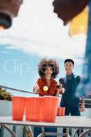 Happy young friends playing beer pong together outside. Diverse friends throwing a ball into cups of beer. Young asian man having fun and playing a game with his hispanic friend.Smiling young friends