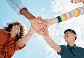 A low close up view of a group of diverse young friends joining hands in a huddle while smiling with a blue sky in the background on a sunny day. Mixed race female with a cool afro hairstyle and her