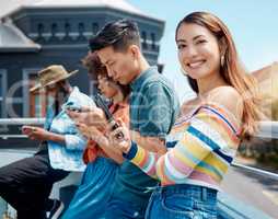 Portrait of beautiful young smiling asian woman standing outside with friends and using her cellphone to browse the internet. Group of diverse millennials using their phones to connect to social medi