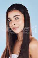 Portrait of one beautiful young hispanic woman with healthy skin and sleek long hair smiling against a blue studio background. Happy mixed race model with flawless complexion and natural beauty