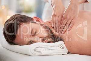 Handsome caucasian man lying on a table at the spa for his back massage. Shirtless man relaxing in a day spa getting pampered by the masseuse. Handsome customer under a towel ready for his rub down